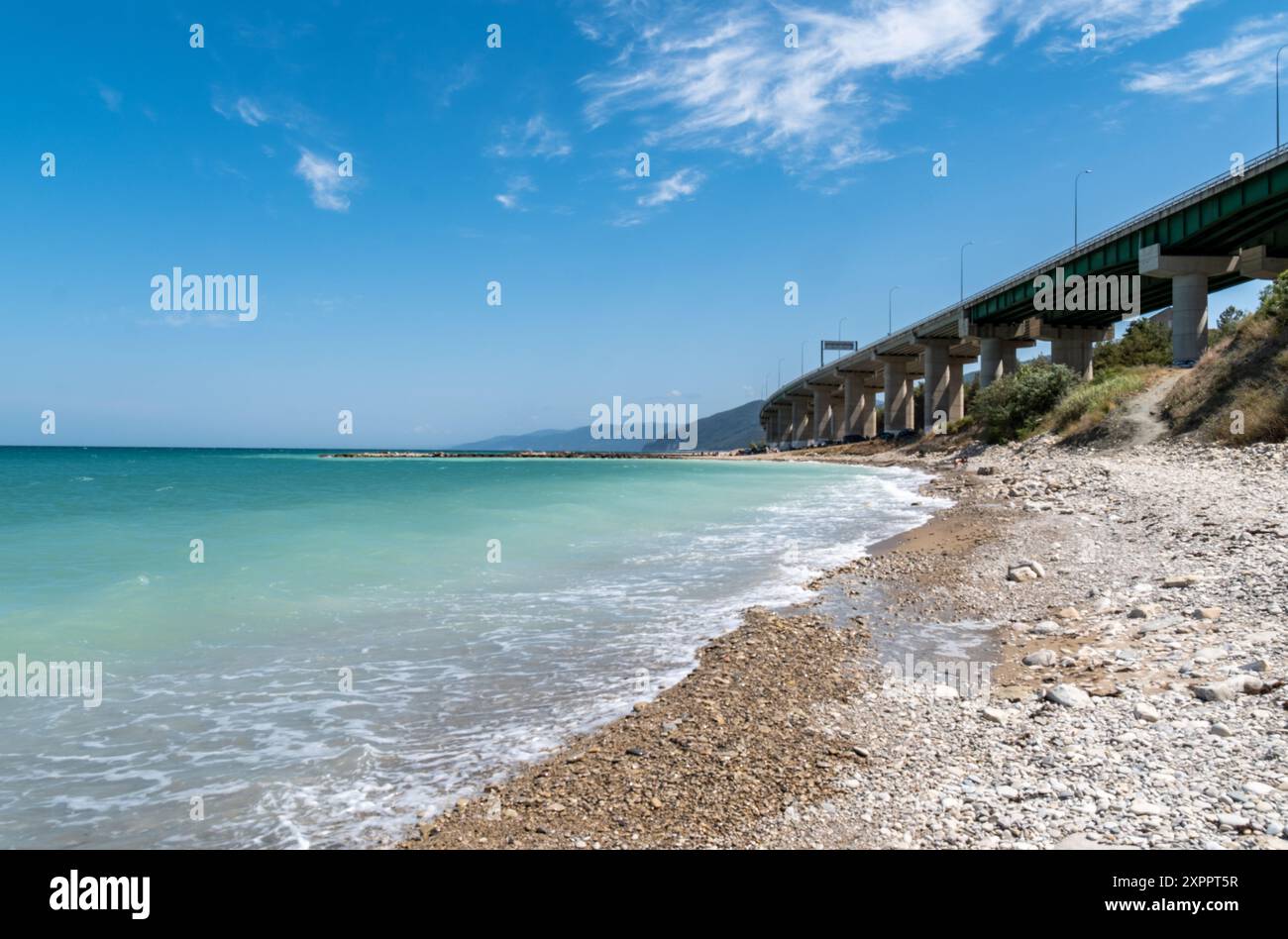 Splendida vista costiera di un ponte che si estende sulle limpide acque blu e sulla spiaggia sabbiosa in una posizione tranquilla sul mare. Foto Stock