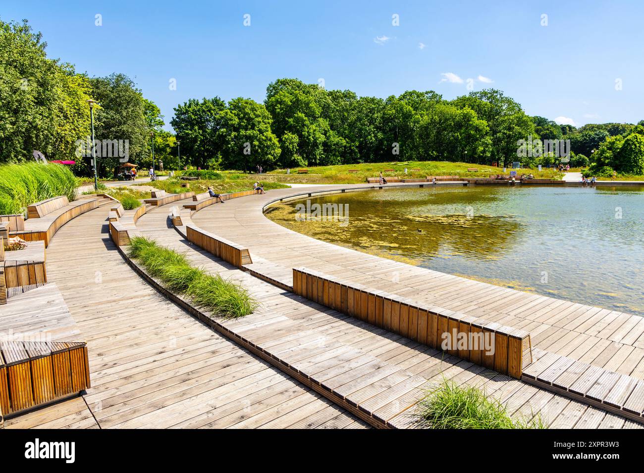 Passerella in legno e posti a sedere intorno allo stagno al parco Pole Mokotowskie, Varsavia, Polonia Foto Stock