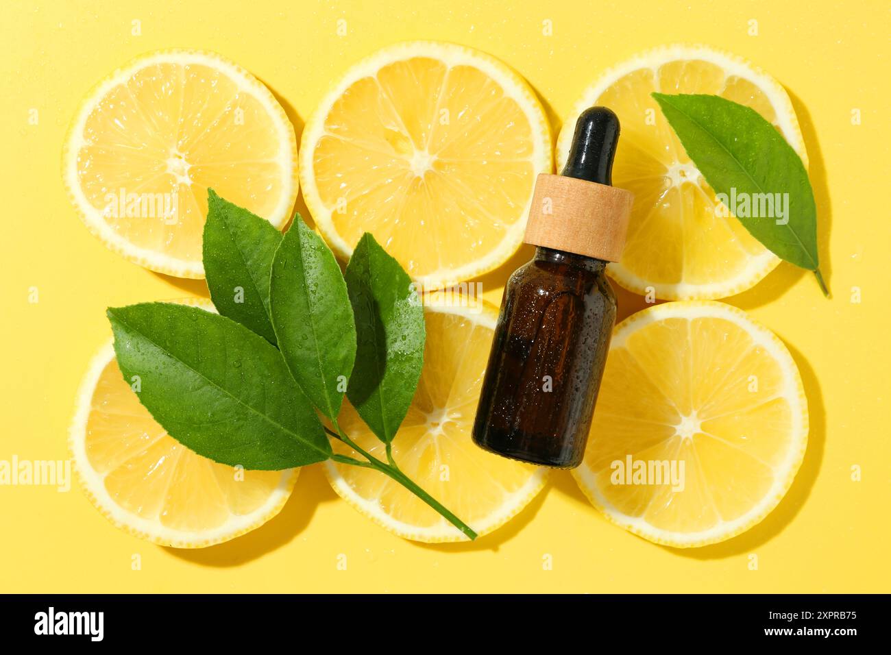 Bottiglia di olio essenziale, foglie di limone e verde su sfondo giallo, piano Foto Stock