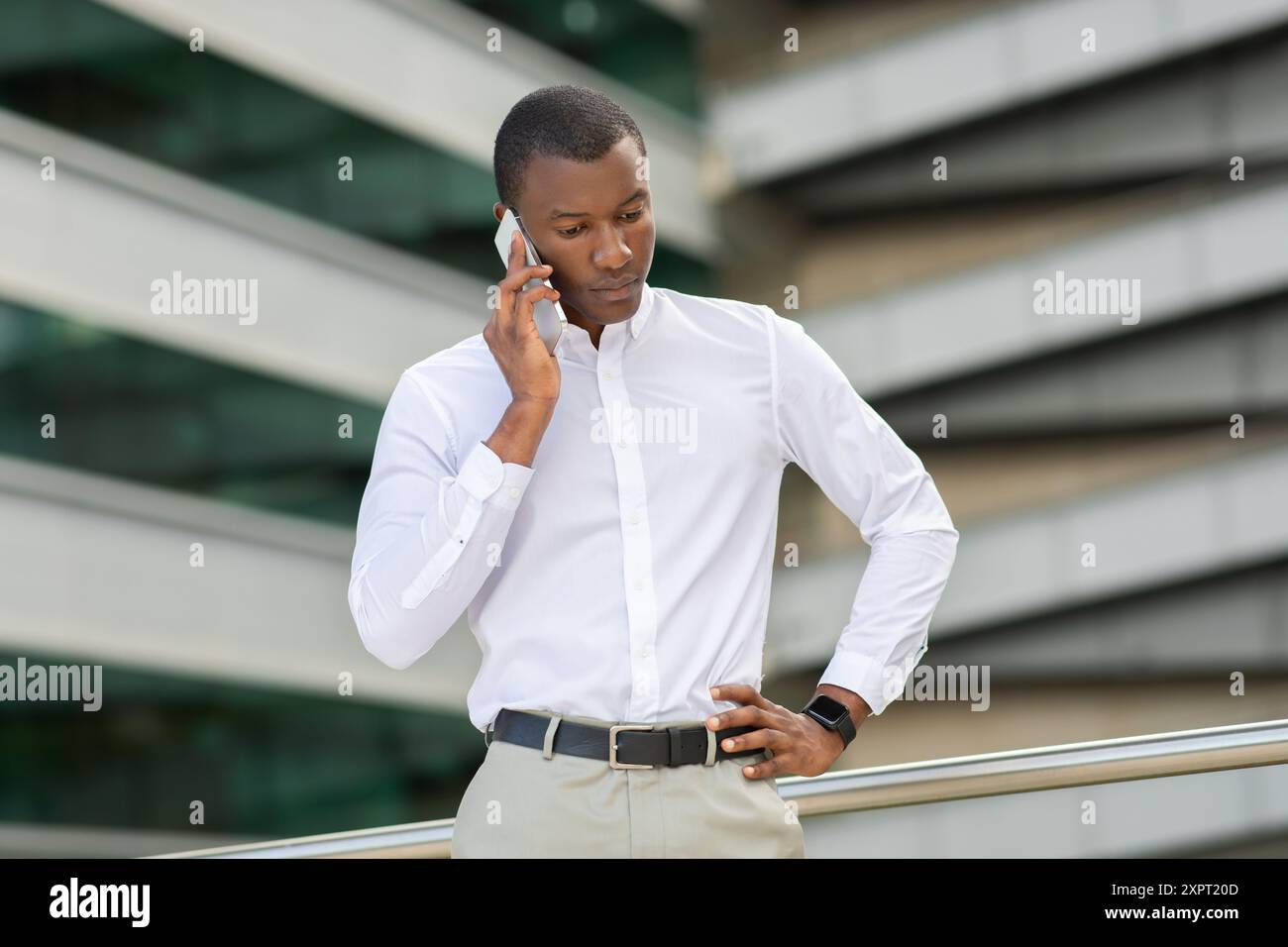 Giovane uomo che indossa una camicia bianca impegnato in una chiamata telefonica seria Foto Stock
