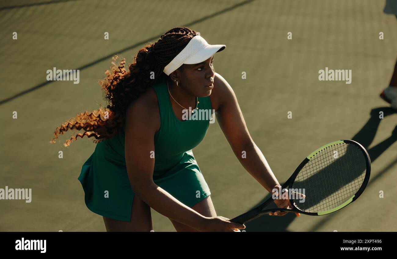 Donna afroamericana che gioca attivamente a tennis su un campo, mostrando il suo atletismo e la sua concentrazione durante la partita. Foto Stock