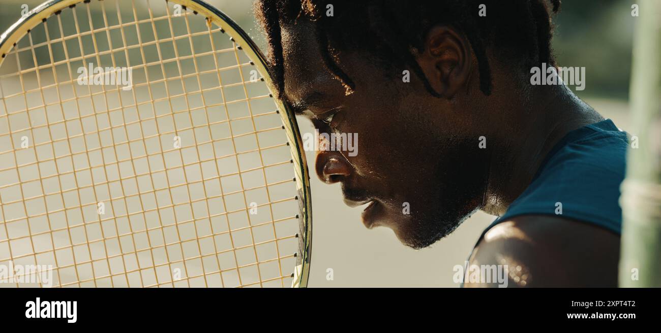 Uomo afro-americano con dreadlock che tiene una racchetta da tennis in modo mirato e determinato. Foto Stock