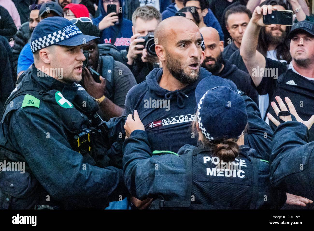 Londra, Regno Unito. 7 agosto 2024. Un uomo si arrabbia con la protesta dicendo che è il suo paese e mostra un tatuaggio di tre leoni sullo stomaco, alla fine viene portato via dalla polizia - A Stop Racism, fermare l'odio e fermare la manifestazione di estrema destra - Una risposta alle attese continue proteste di estrema destra nei centri di asilo e immigrazione o nei loro dintorni - questo caso presso Immigration and Nationality Services Ltd North Finchley. Organizzato dalla SPERANZA, non dall'odio e dalla resistenza al razzismo. Crediti: Guy Bell/Alamy Live News Foto Stock