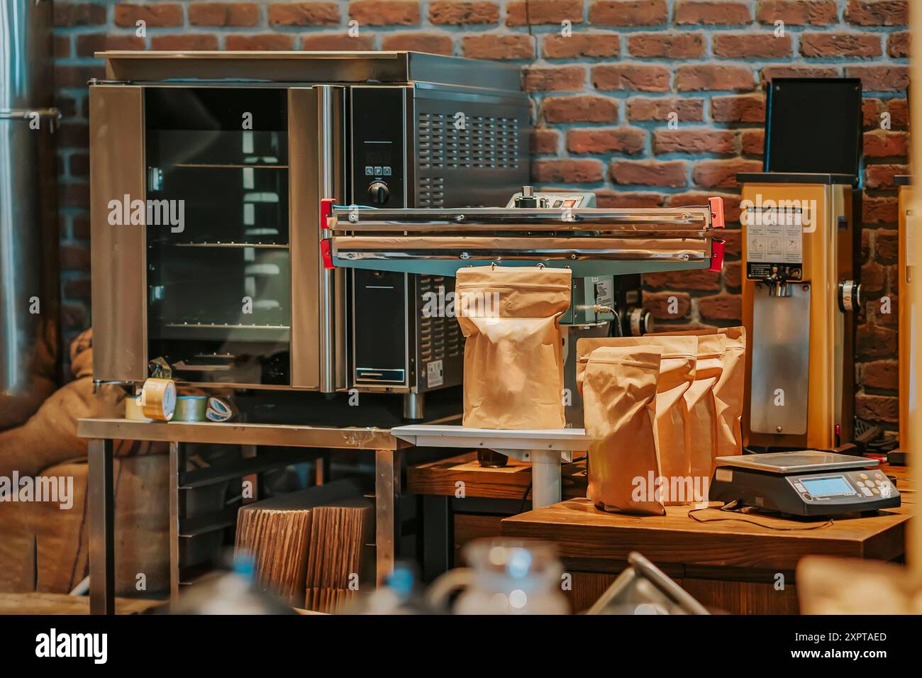 Cucina della caffetteria con attrezzature industriali, tra cui torrefazione, macchina sigillante e sacchetti di chicchi di caffè, pronti per l'imballaggio Foto Stock