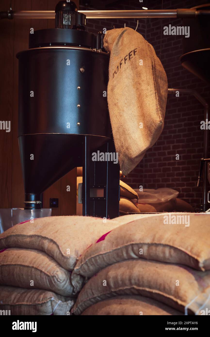 Attrezzature per la torrefazione del caffè e sacchetti Burlap pieni di chicchi di caffè nel magazzino della caffetteria Foto Stock