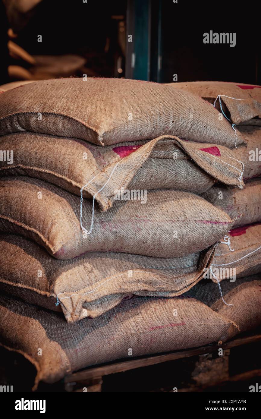 Pile di sacchi di burlap pieni di chicchi di caffè vengono immagazzinati in un magazzino Foto Stock