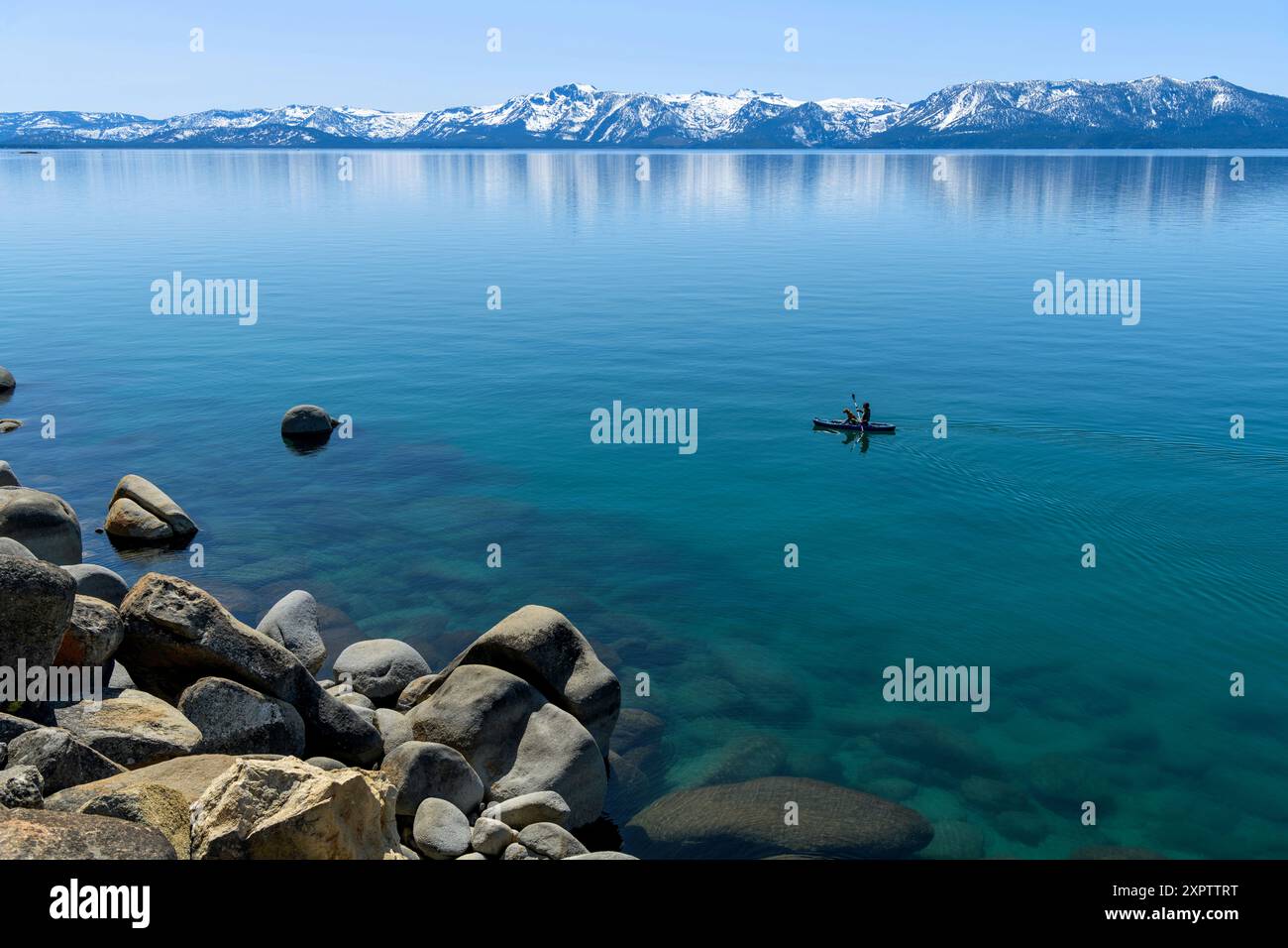 Kayak sul lago Blue Mountain - Una crociera in kayak sulle acque cristalline del lago Tahoe, con cime innevate che torreggiano a riva, CA-NV, Stati Uniti. Foto Stock