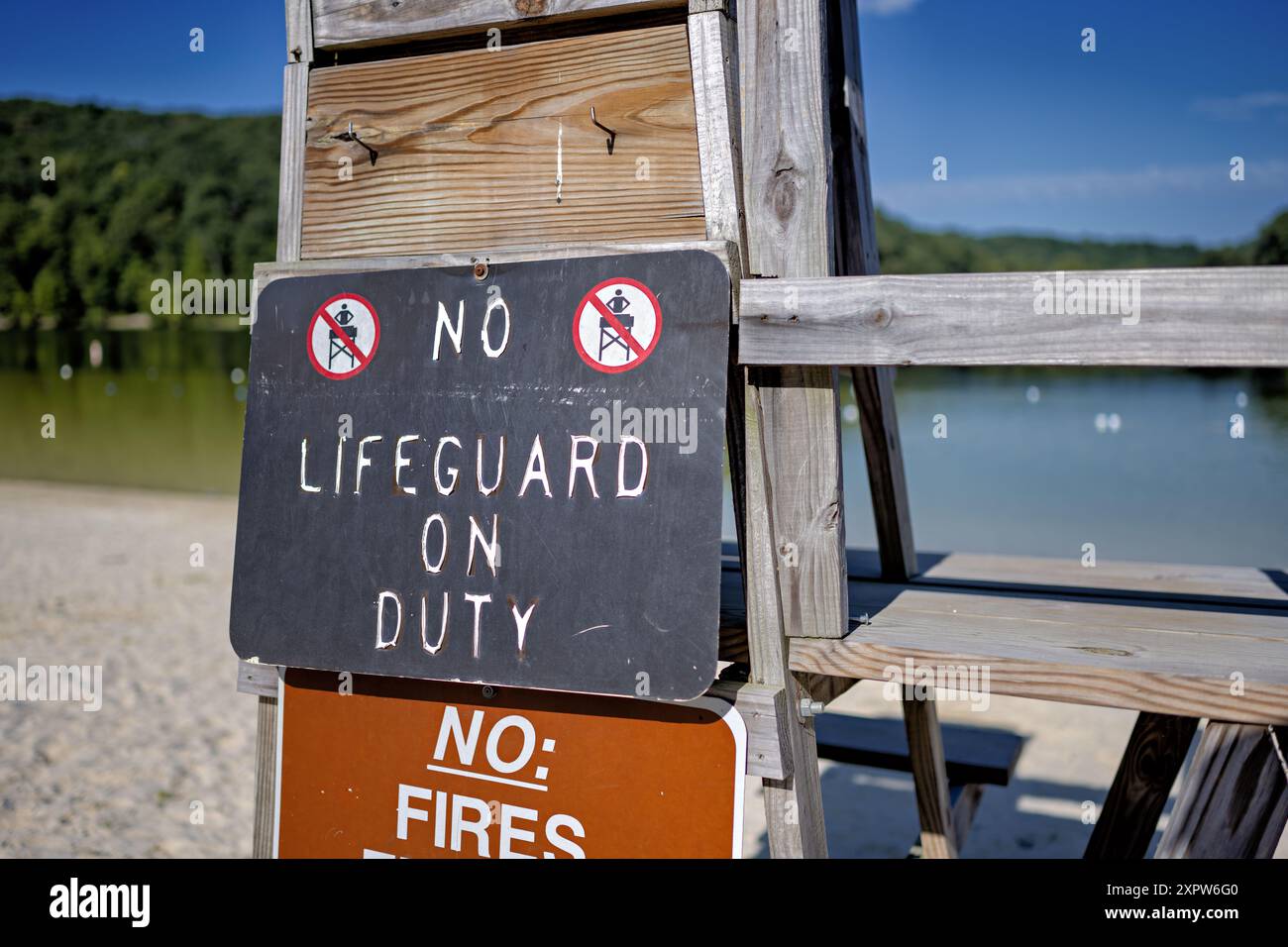 Bagnino Stand No bagnino in servizio cartello Greenbrier Lake Boonsboro Maryland // BOONSBORO, Maryland, Stati Uniti - un vecchio banco bagnino in legno con un cartello "No bagnino in servizio" presso il lago Greenbrier vicino a Boonsboro, Maryland. Questa scena estiva cattura il fascino rustico della zona del lago in una giornata di sole, con le calme acque del lago visibili sullo sfondo. Foto Stock