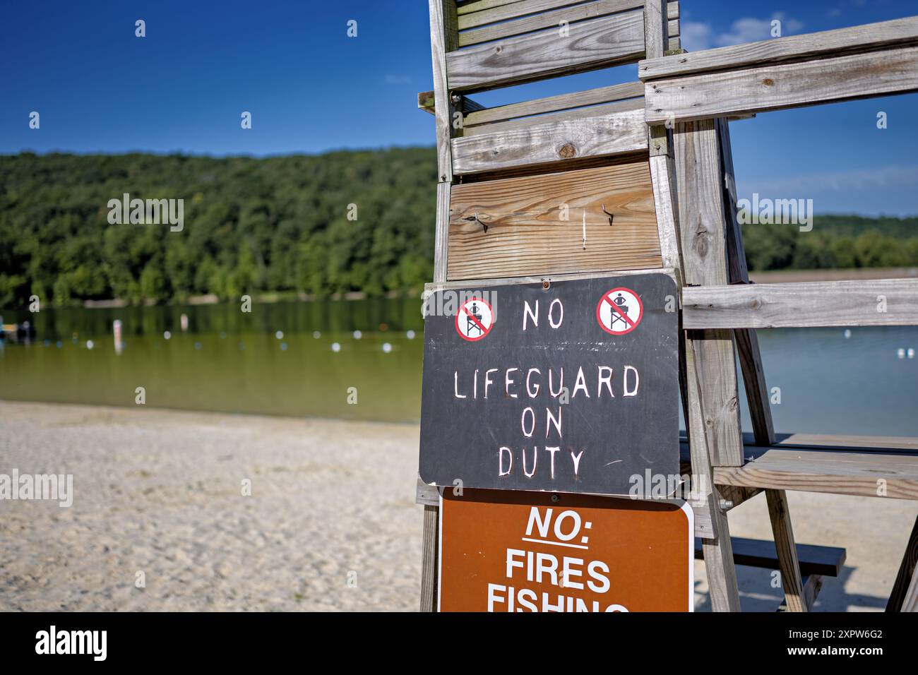 Bagnino Stand No bagnino in servizio cartello Greenbrier Lake Boonsboro Maryland // BOONSBORO, Maryland, Stati Uniti - un vecchio banco bagnino in legno con un cartello "No bagnino in servizio" presso il lago Greenbrier vicino a Boonsboro, Maryland. Questa scena estiva cattura il fascino rustico della zona del lago in una giornata di sole, con le calme acque del lago visibili sullo sfondo. Foto Stock
