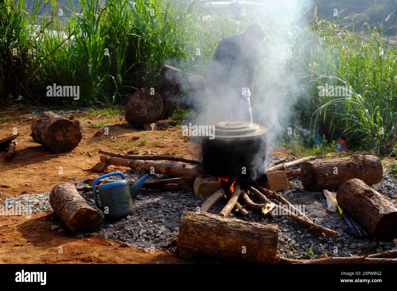 Una pentola nera fumante all'aperto sul fuoco di una stufa improvvisata fatta di mattoni e pietre, circondata dalla natura, come un tradizionale cuoco vietnamita banh tet Foto Stock