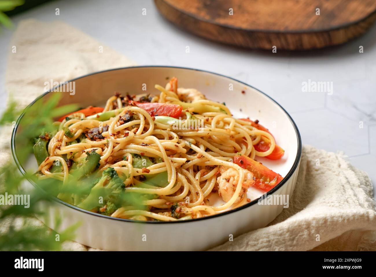 Pasta fritta in padella con gamberi, broccoli, funghi e pomodoro. Servita su un piatto bianco. Foto Stock