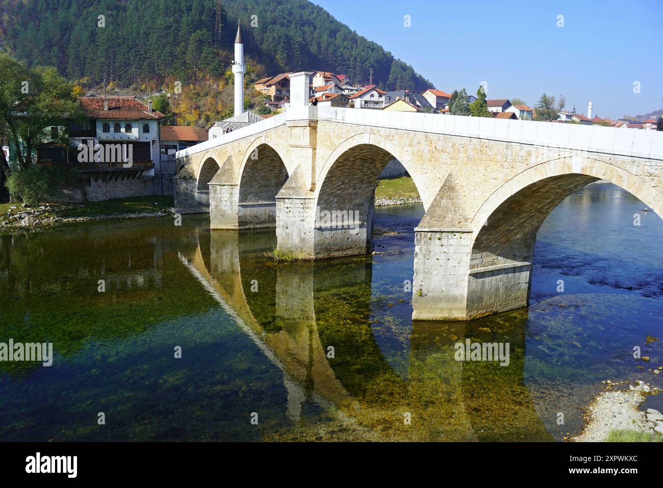 Vecchio ponte ad arco sullo sfondo di una montagna boscosa ed edifici nella parte storica di Konjic. Stara Ćuprija sul fiume Neretva. Foto Stock