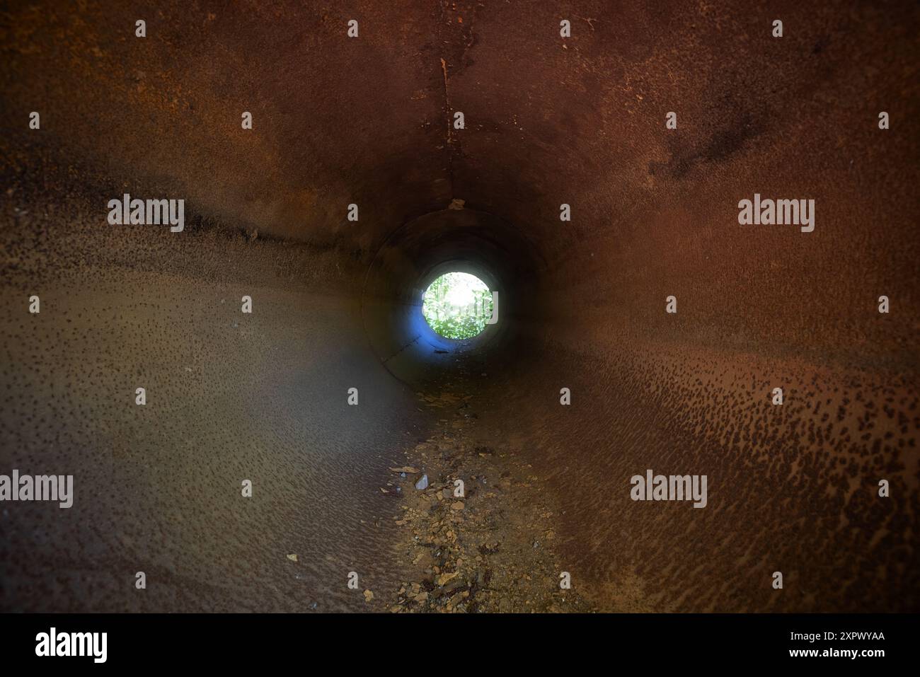 Vista prospettica del tunnel di un tubo in acciaio arrugginito con estremità luminosa Foto Stock
