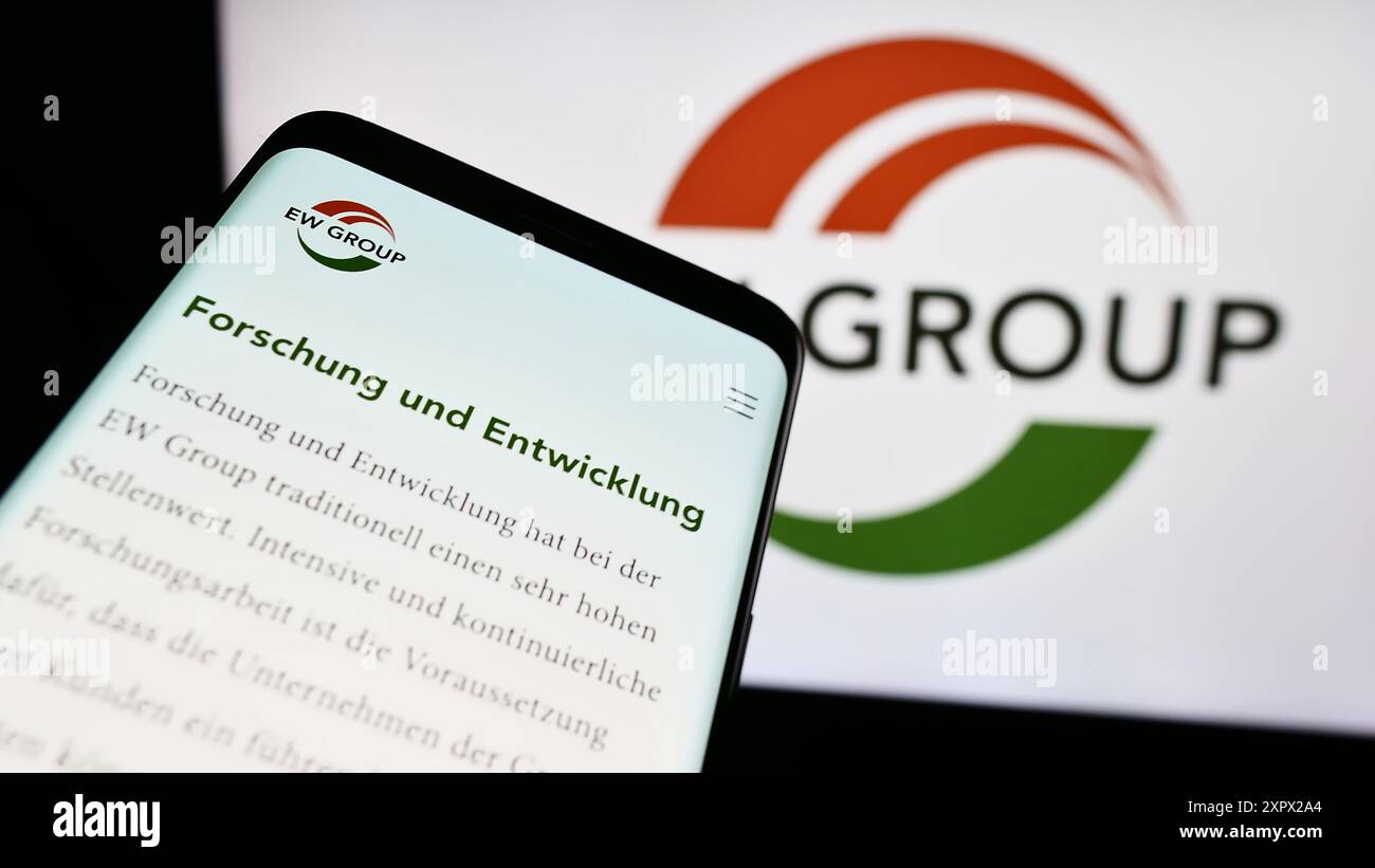 Telefono cellulare con sito web della società tedesca di allevamento EW Group GmbH davanti al logo aziendale. Mettere a fuoco in alto a sinistra sul display del telefono. Foto Stock