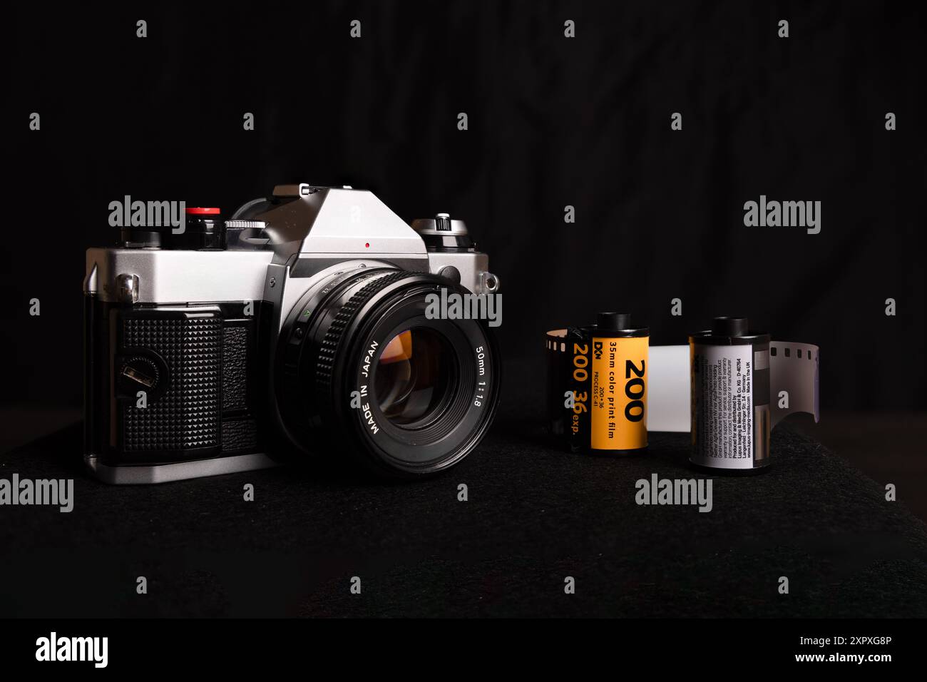 Ripresa dettagliata di una vecchia macchina fotografica insieme a rotoli di pellicola da 35 mm, su uno sfondo nero, con attrezzature fotografiche d'epoca. Foto Stock
