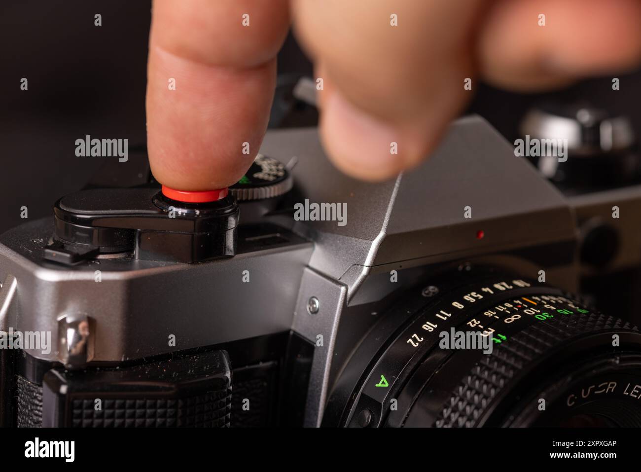 Un primo piano di una vecchia videocamera con un dito sul pulsante dell'otturatore, in contrasto con uno sfondo scuro. Intramontabile e suggestivo. Foto Stock