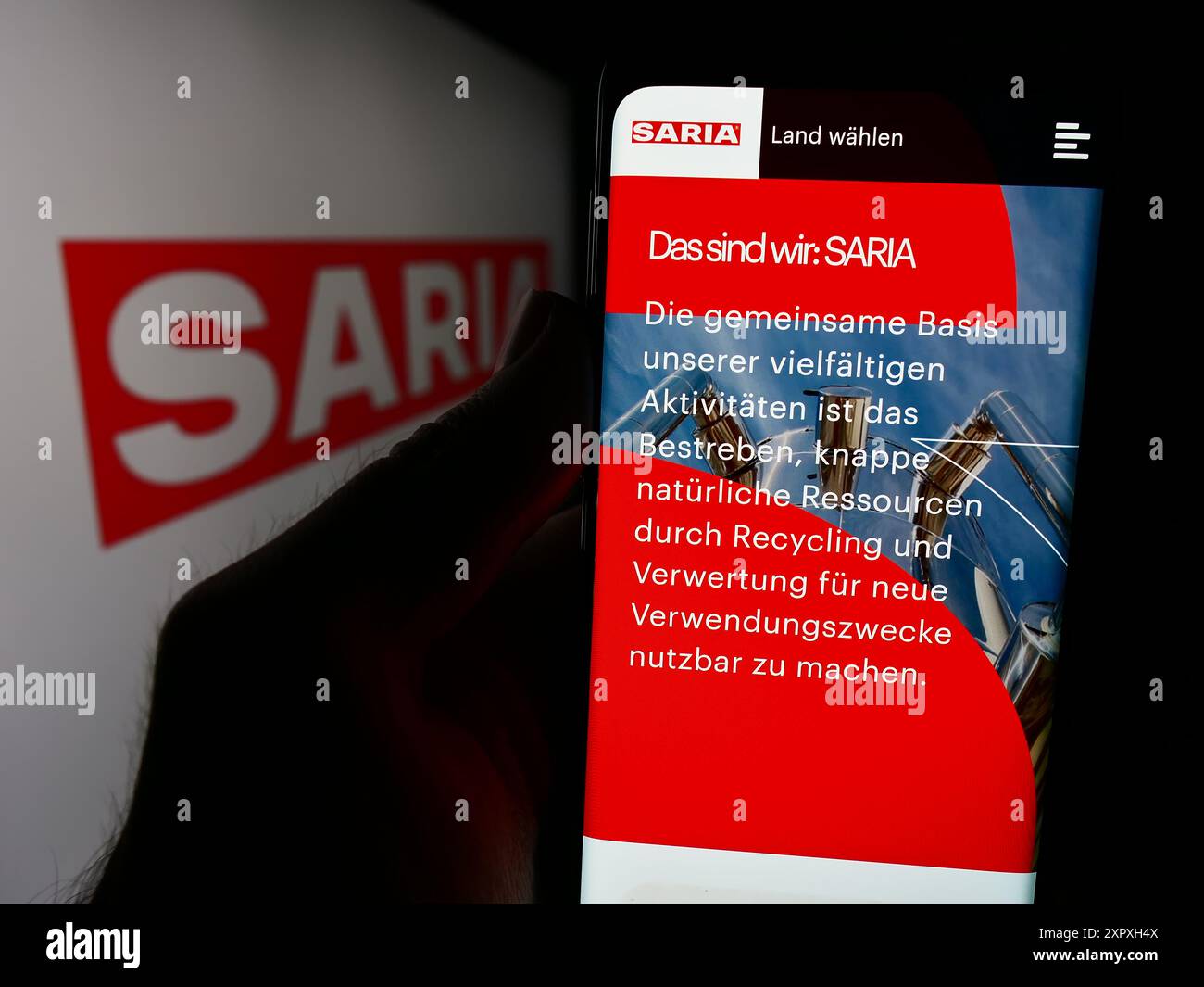 Persona che detiene un cellulare con pagina web della società alimentare tedesca Saria AS GmbH Co. KG davanti al logo. Messa a fuoco al centro del display del telefono. Foto Stock
