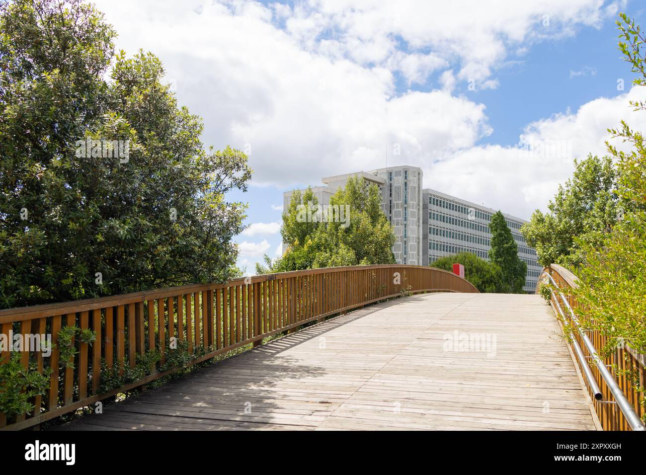 Ponte ciclabile in legno che conduce ad un moderno edificio di uffici con un cielo blu luminoso e nuvole bianche a lisbona, portogallo Foto Stock