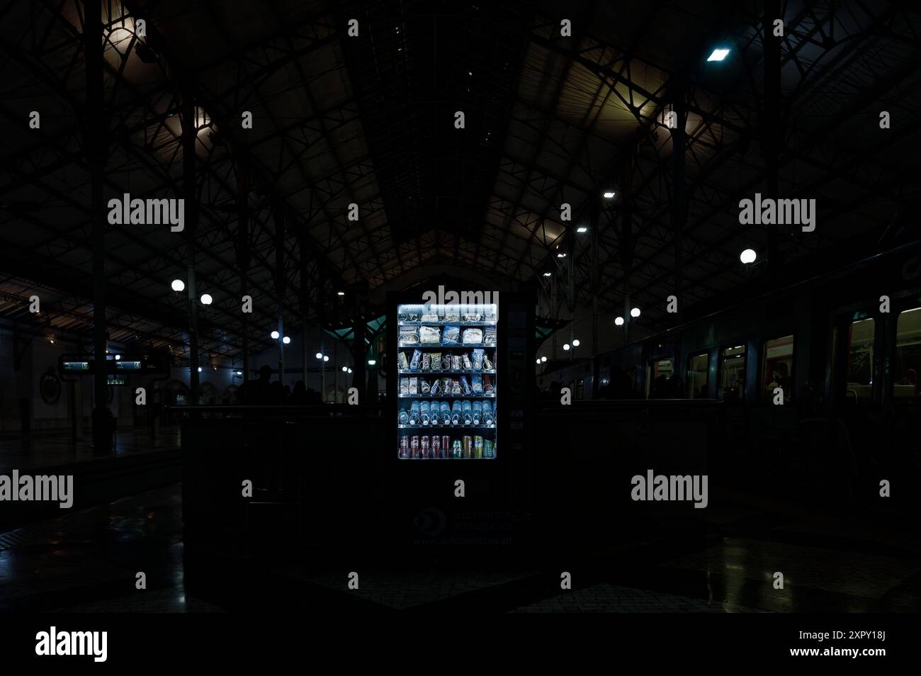 Un distributore automatico brilla di luce nella stazione ferroviaria di Rossio, poco illuminata, catturando un momento di tranquillità nel vivace centro di transito di Lisbona Foto Stock