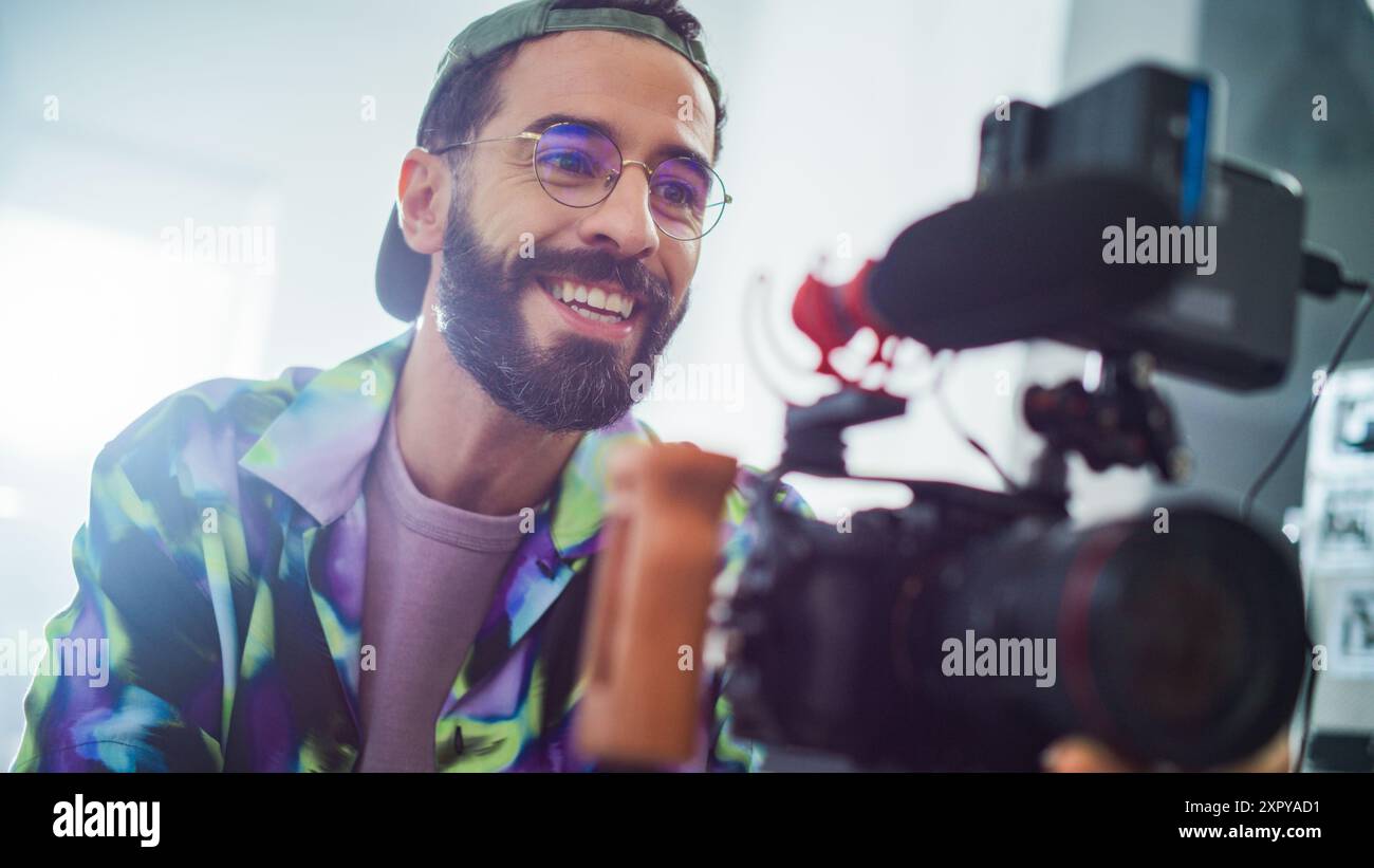 Giovane Filmmaker latino che gestisce Una fotocamera professionale in Uno studio ben illuminato, catturando contenuti coinvolgenti per Un moderno progetto di pubblicità o produzione cinematografica. Foto Stock