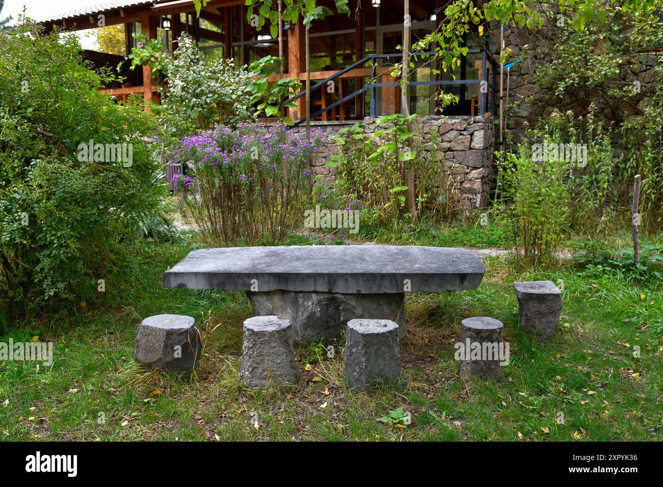 Un tavolo in pietra con sgabelli coordinati si trova in mezzo a una vibrante vegetazione autunnale. Foto Stock