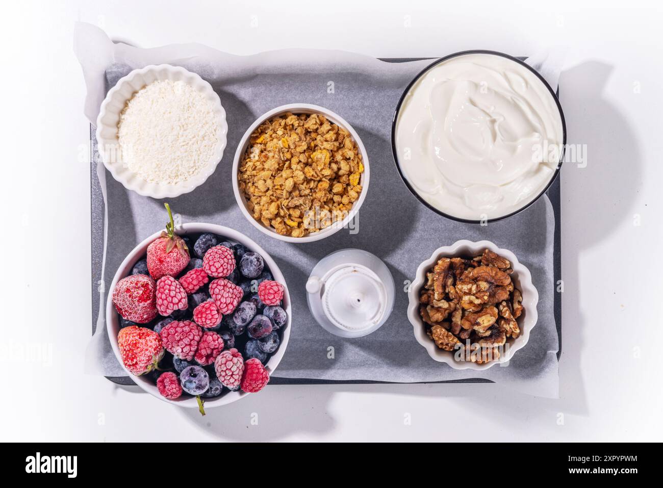 Preparazione della cottura con sfondo di corteccia di yogurt congelato con yogurt greco, bacche fresche, muesli, miele, salsa al cioccolato, con vassoio da forno deco. Vista dall'alto della donna Foto Stock