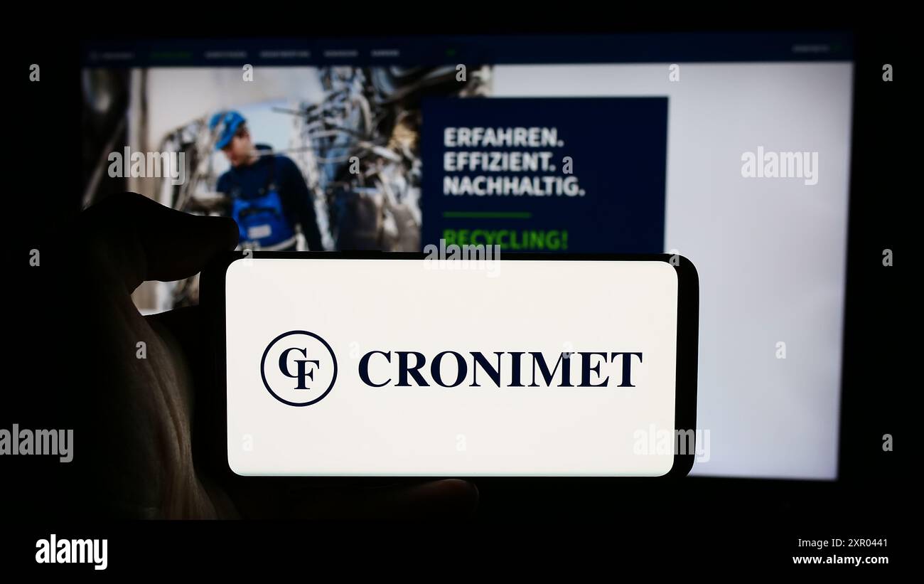 Persona che detiene un cellulare con il logo della società tedesca di riciclaggio dei metalli Cronimet Holding GmbH davanti alla pagina web aziendale. Mettere a fuoco il display del telefono. Foto Stock