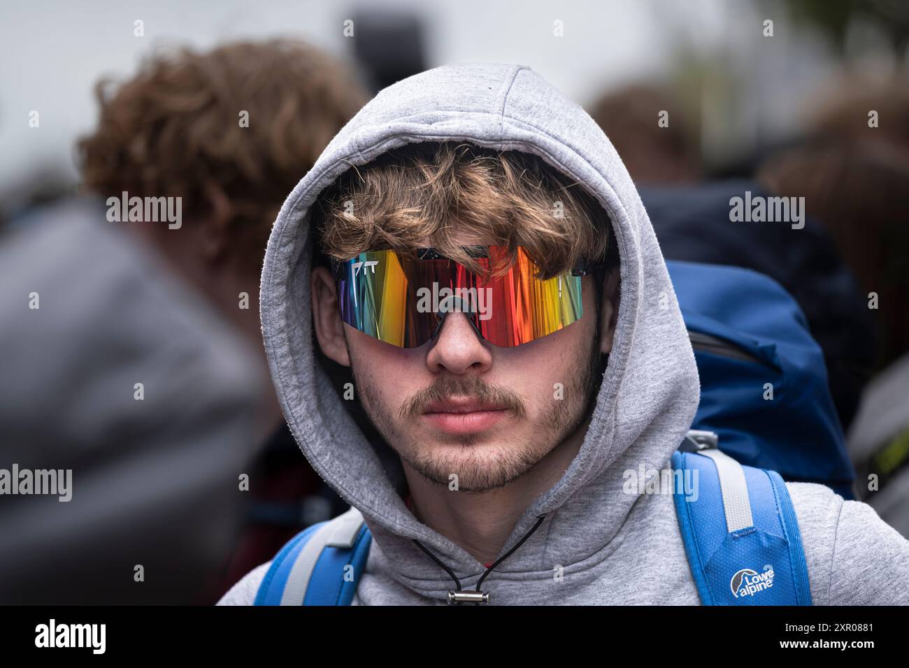 Un giovane uomo che indossa un paio di occhiali da sole con cappuccio e visiera che guarda la fotocamera a Newquay, in Cornovaglia, nel Regno Unito. Foto Stock