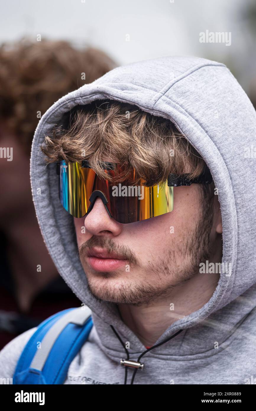 Un giovane uomo che indossa un paio di occhiali da sole con cappuccio e visiera che guarda la fotocamera a Newquay, in Cornovaglia, nel Regno Unito. Foto Stock