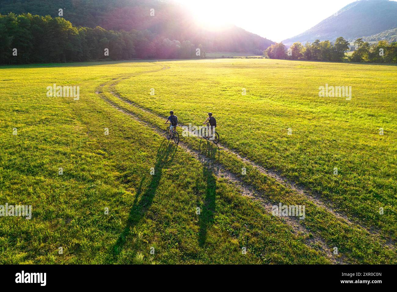 Turisti, coppie in mountain bike, ciclisti su una strada sterrata in bicicletta attraverso un bellissimo prato contro il sole del tramonto, Dolenjske toplice, Slovenia Foto Stock