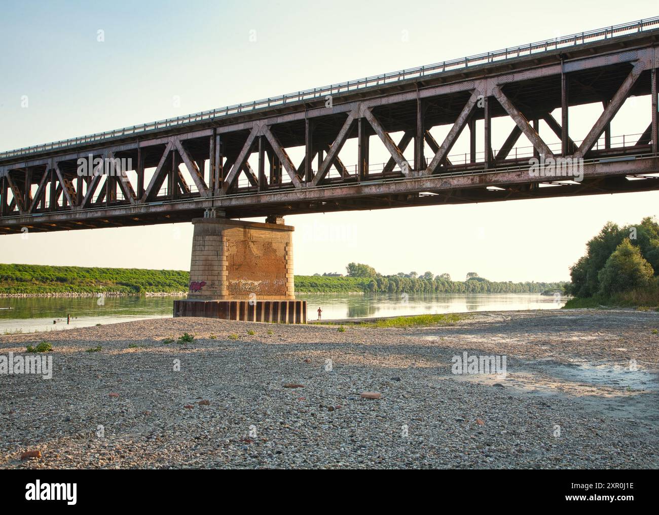 Paesaggio con il po nella stagione estiva con un uomo che pesca da solo sotto il ponte della ferrovia, vicino a Pavia, Italia. Foto Stock