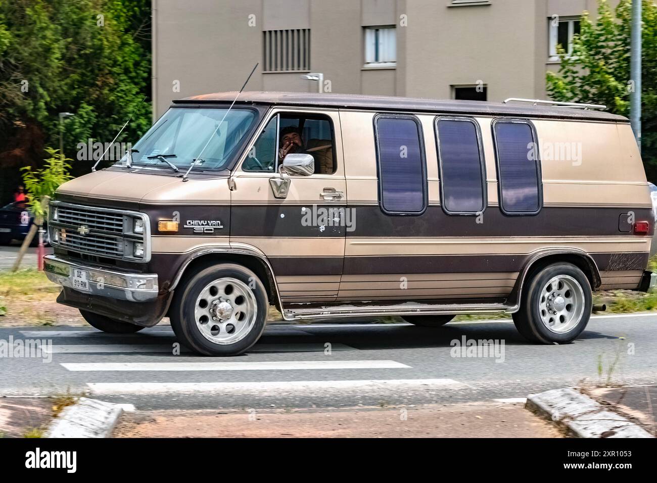 chevrolet chevy van G20 americano vintage marrone e beige in Francia che guida su una strada della città con alberi ed edifici sullo sfondo Foto Stock