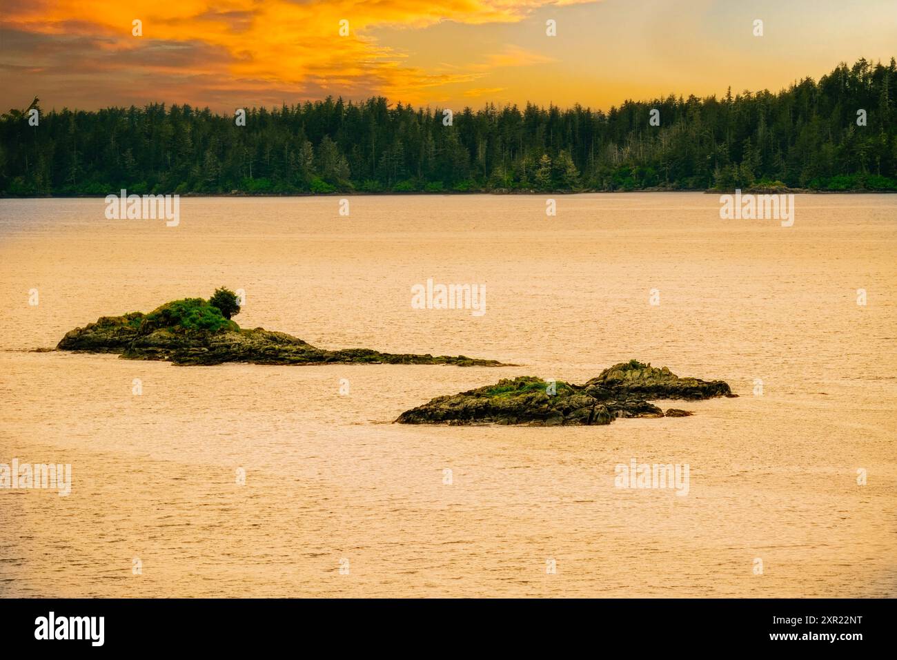 Tramonto nella terra del sole di mezzanotte, due piccole isole e la terraferma oltre sotto il cielo arancione, giallo e blu con nuvole colorate. Foto Stock