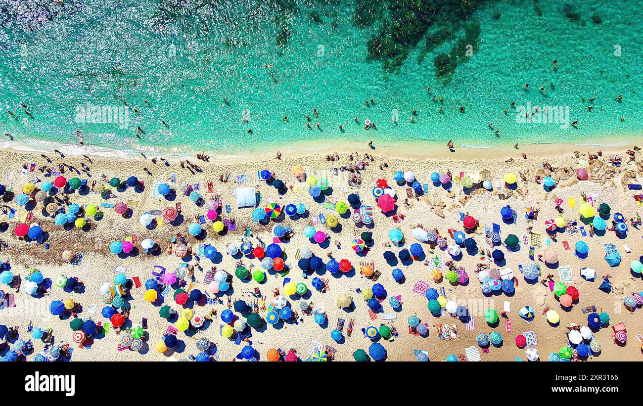 Überfüllter Strand, bunte Sonnenschirme, klares türkisfarbenes Wasser, Menschen im Wasser, Sonnenbaden, Sommerurlaub, Hitzewelle, Tourismus, Klimawandel, Nachhaltigkeit, Erderwärmung, Wasserknappheit, Umweltbelastung, Naturerlebnis, Sonnenschein, Dürre, Übernutzung von Ressourcen, Sommerhitze, Erholung, Überfüllung Plastikverschmutzung, Mikroplastik, Meeresschutz, Küstenerosion, steigende Meeresspiegel, Hitzenotstand, Gesundheitsrisiken, Klimakrise, Schutzmaßnahmen, Urlauber, Reise, Symbolfoto *** Spiaggia affollata, ombrelloni colorati, acque turchesi limpide, gente in acqua, prendere il sole, sommare Foto Stock