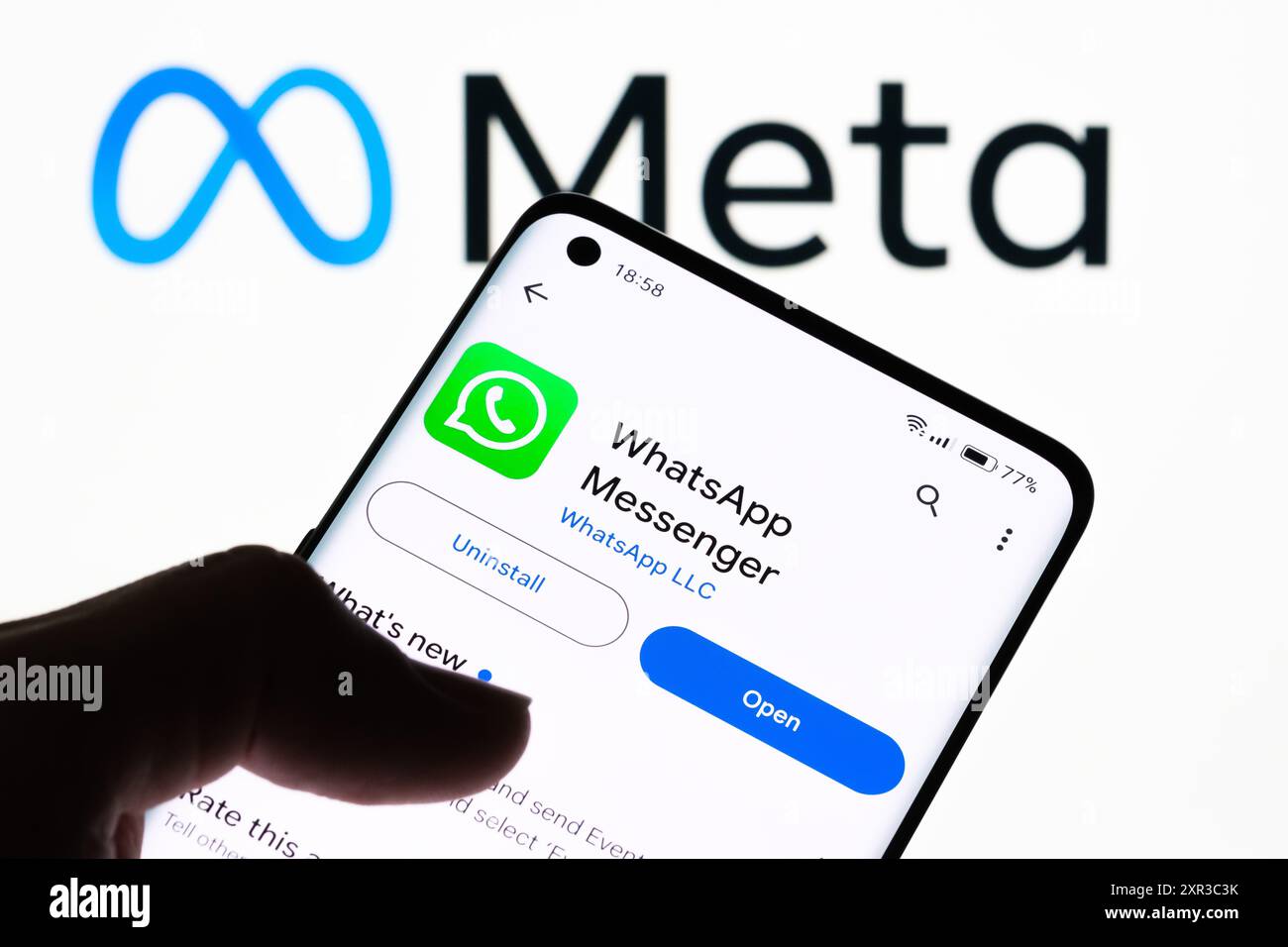 Primo piano dello schermo di uno smartphone che visualizza l'app WhatsApp Messenger con il logo Meta sullo sfondo, a dimostrazione della relazione tra WhatsApp e Foto Stock