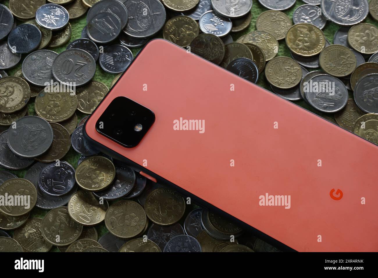 Terengganu, Malesia - 24 agosto 2024: Primo piano dello smartphone google pixel 4 arancione sulle monete malesi sparse Foto Stock