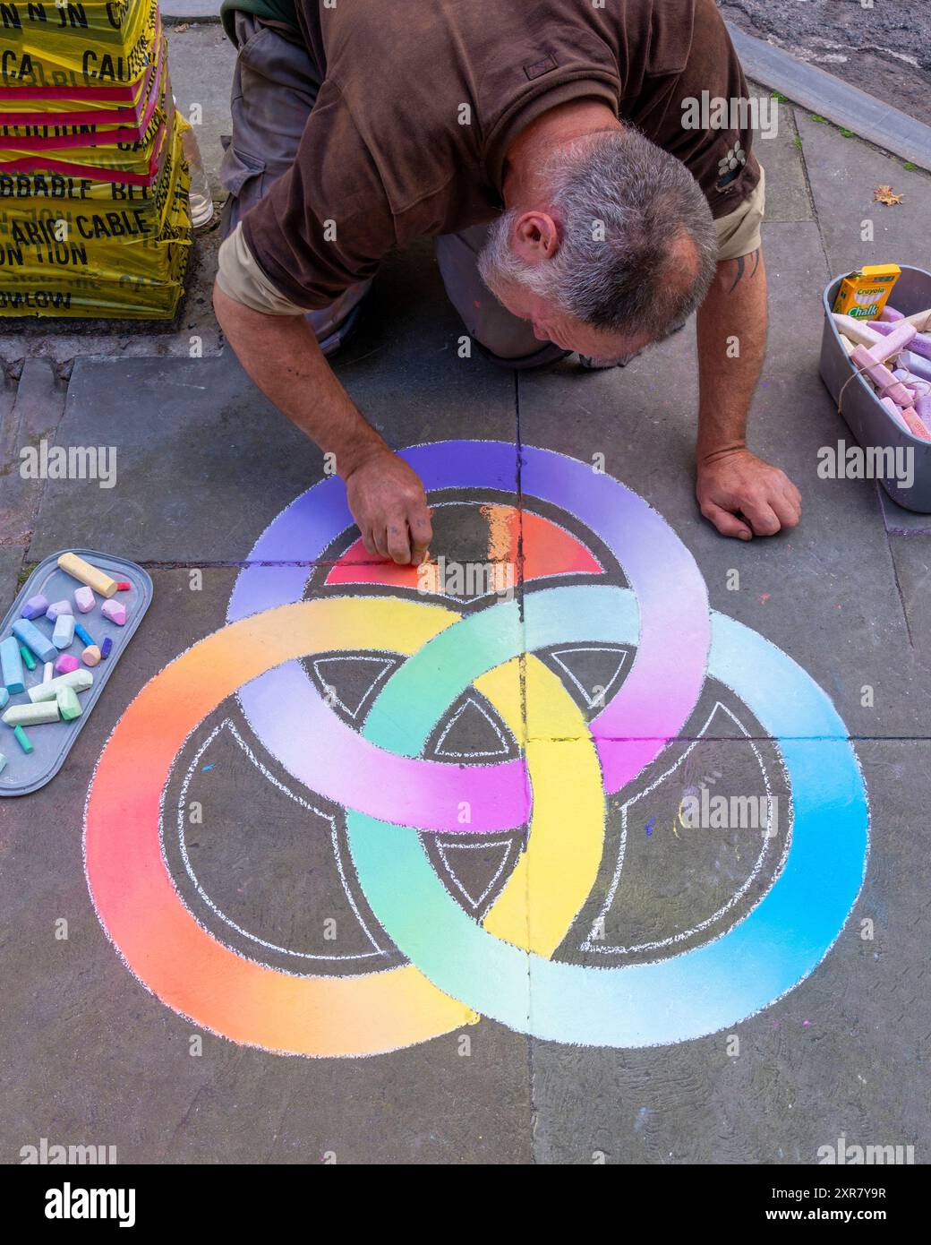 Artista di strada maschile che disegna un "mandala di gesso"- anelli borromei (che indicano la forza in unità).sul pavimento Glastonburys, Foto Stock