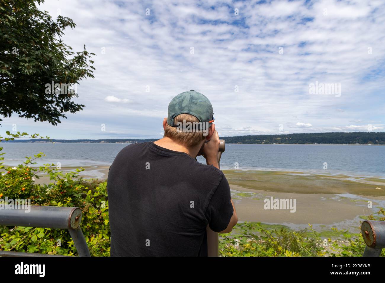 Uomo che guarda attraverso un binocolo sulla costa di Whidbey Island Foto Stock