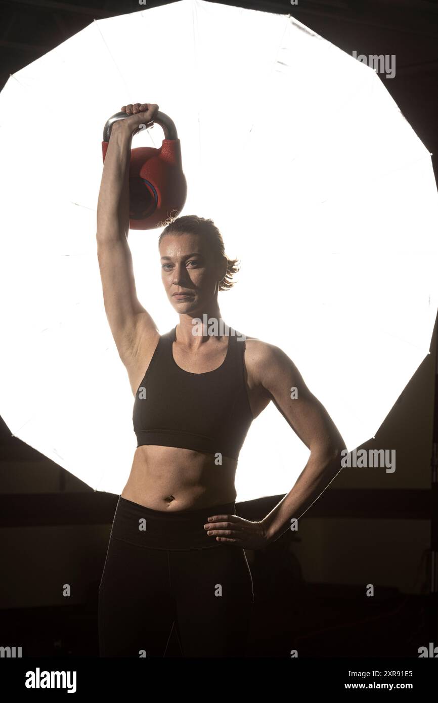 La donna posa con il kettlebell davanti alla luce Foto Stock