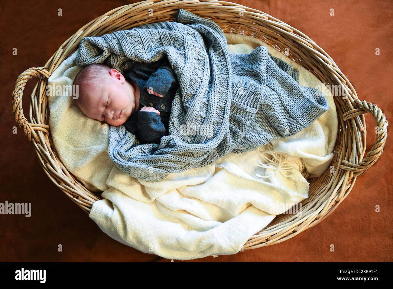 Neonato in abito grigio che dorme in un cestino di vimini con una k Foto Stock