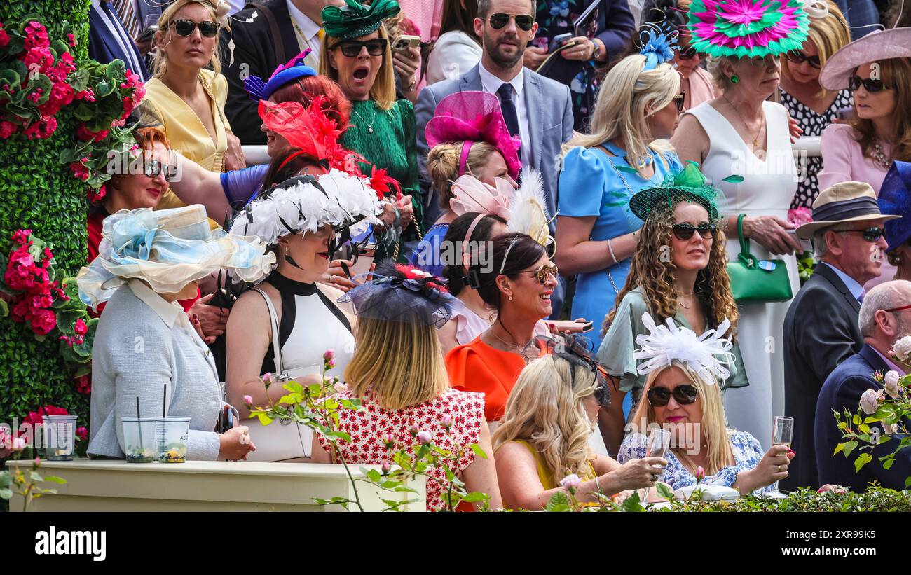 Gli appassionati di corse e gli spettatori in cappelli, abiti e cappelli ammirano la Royal Procession al Royal Ascot, Berkshire Foto Stock