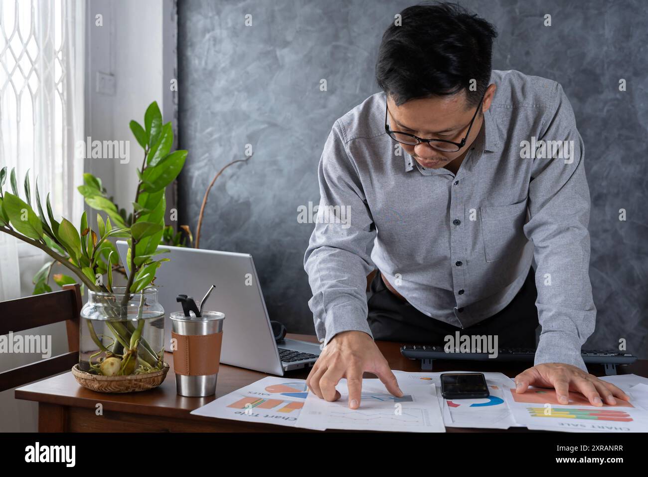 Uomo soddisfatto che legge documenti cartacei, lettera che riceve buone notizie, lavora con un portatile in ufficio seduto sul tavolo, uomo d'affari di successo, libero professionista Foto Stock