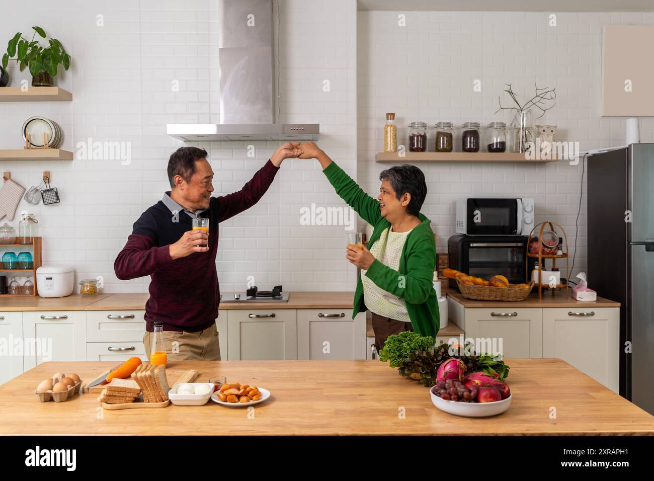 Felice marito anziano e moglie che si divertono negli utensili da cucina, cucinano insieme a casa, sono molto contenti che ci siano adulti maturi. A capelli grigi, ener Foto Stock