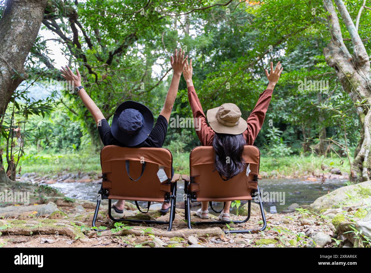 Vista posteriore di una giovane coppia seduta nella loro splendida natura. Coppia seduta su una sedia tenendosi per mano e godendo di una splendida vista sulle montagne Foto Stock