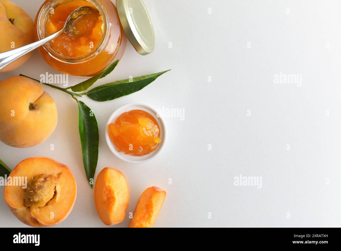 Vasetti con marmellata di pesca isolati su un tavolo bianco con frutta intorno e foglie. Vista dall'alto. Foto Stock