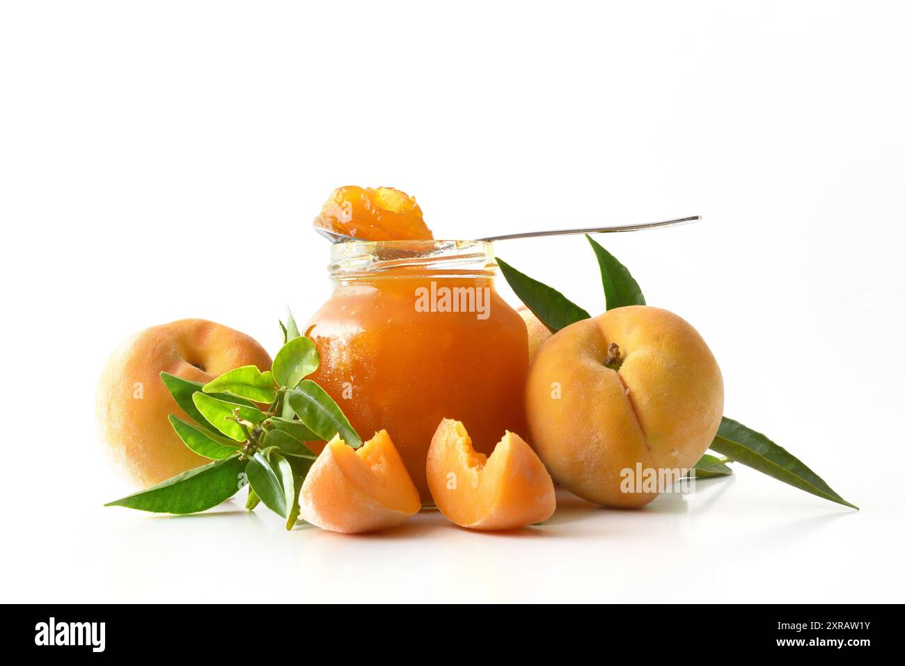 Barattolo di marmellata di pesca isolato su fondo bianco con frutta intorno e cucchiaio riflesso sulla base. Vista frontale. Foto Stock
