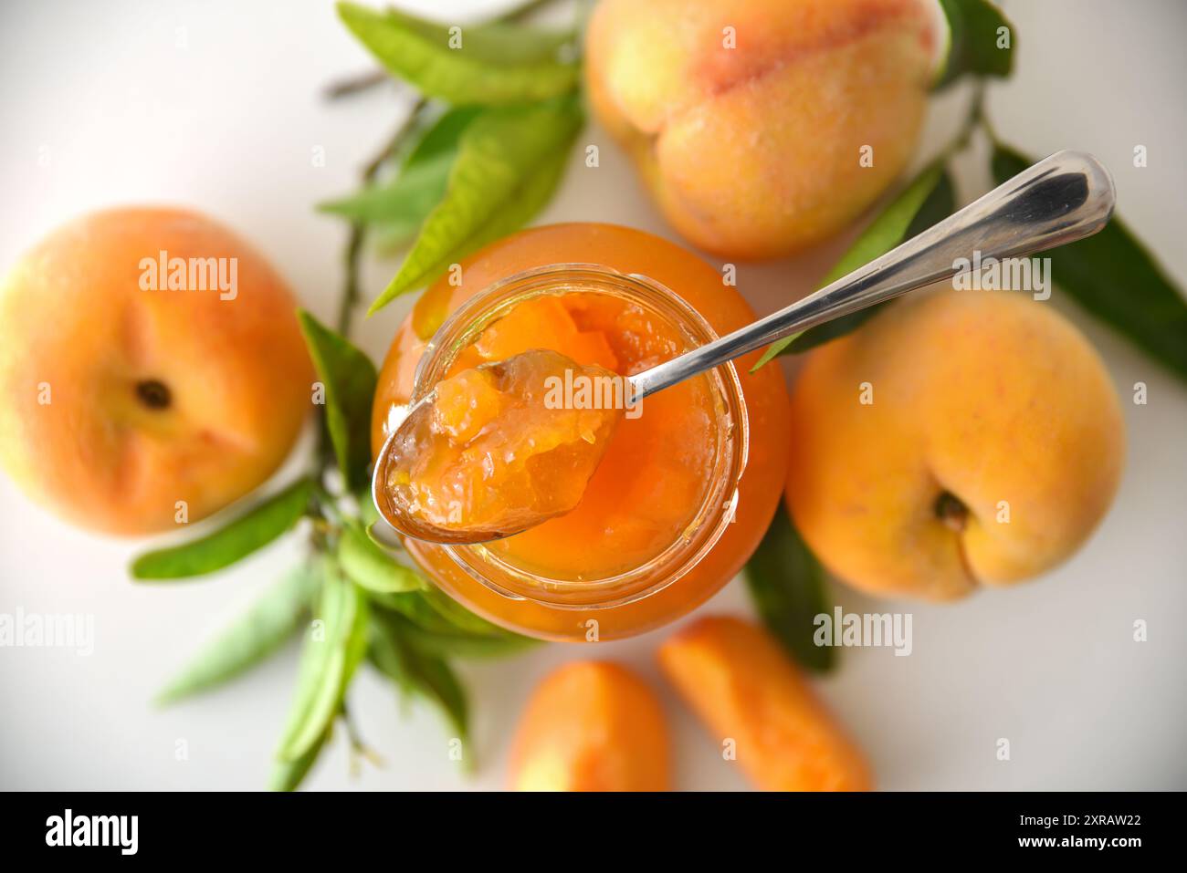 Barattolo di marmellata di pesca isolato su un tavolo bianco con frutta intorno e cucchiaio. Vista dall'alto. Foto Stock