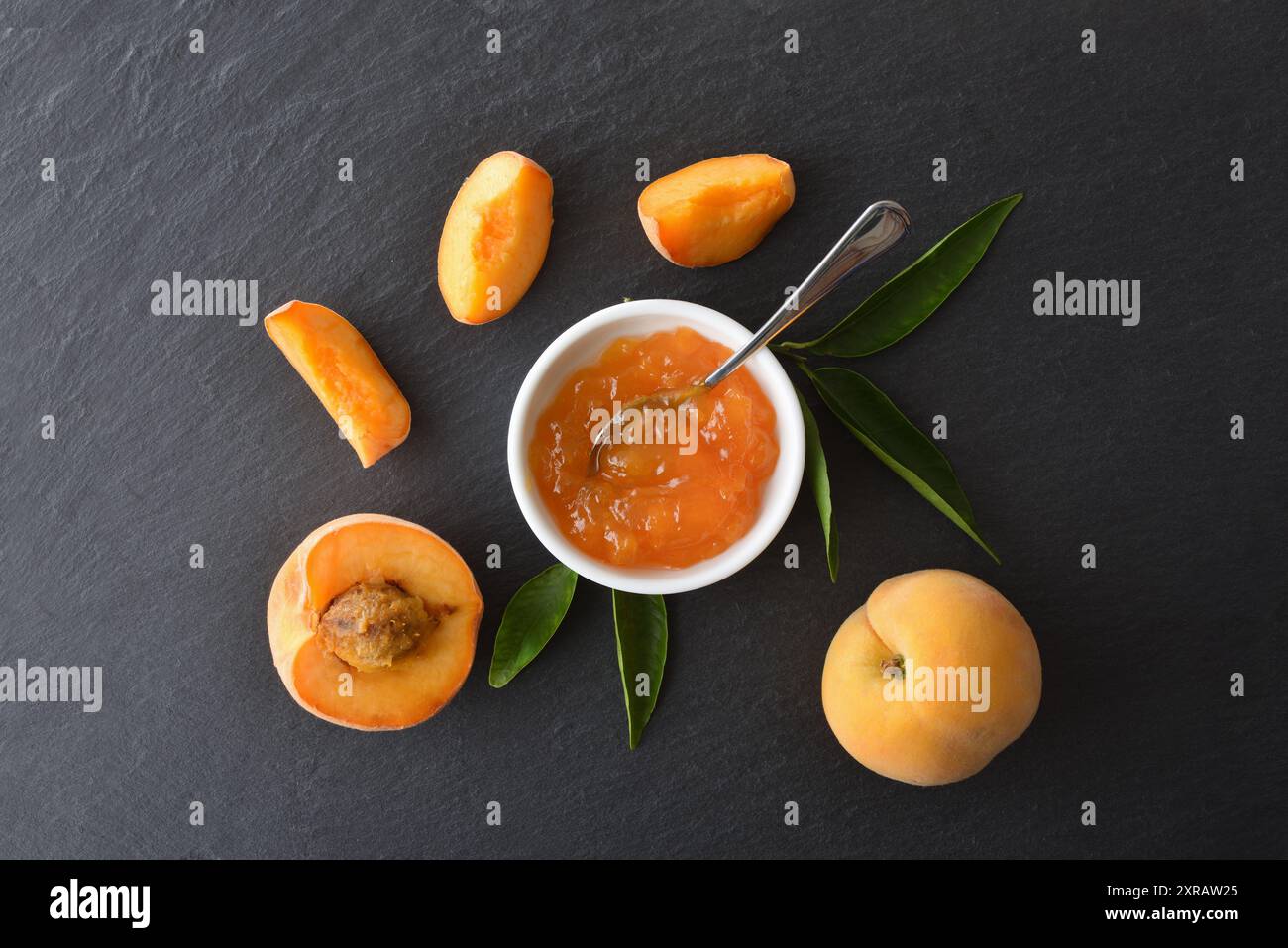 Dettaglio di un piccolo piatto con marmellata di pesca su un banco bianco con frutta e foglie intorno ad esso. Vista dall'alto. Foto Stock