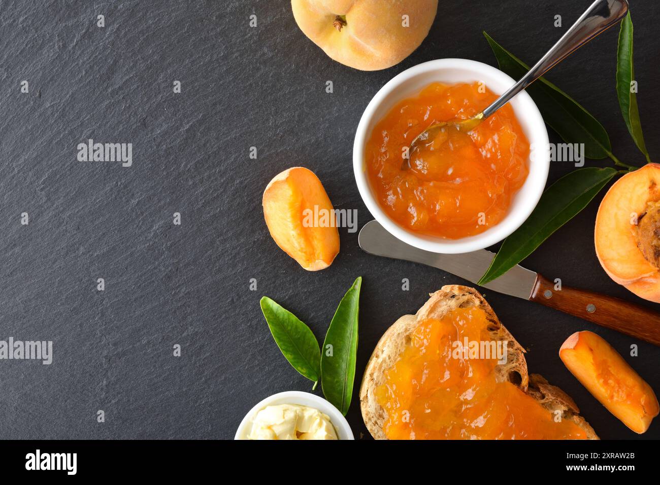 La prima colazione è servita con marmellata di pesca in una ciotola di ceramica bianca, spalmata su una fetta di pane con la frutta intorno su un piatto di ardesia. Vista dall'alto. Foto Stock