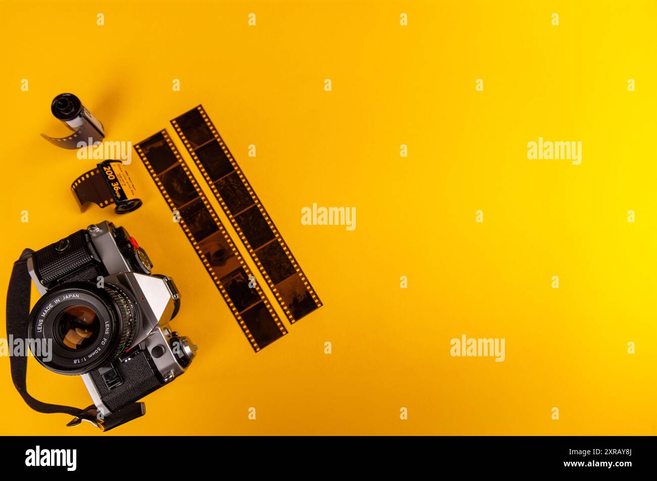 Primo piano di una vecchia fotocamera con rotoli di pellicola da 35 mm allineati in modo ordinato nell'angolo inferiore sinistro su uno sfondo giallo brillante. Un cenno alla fotografia analogica. Foto Stock